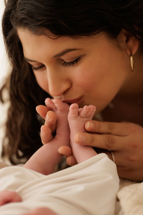 A mother kissing her newborn's feet, held together in her hand