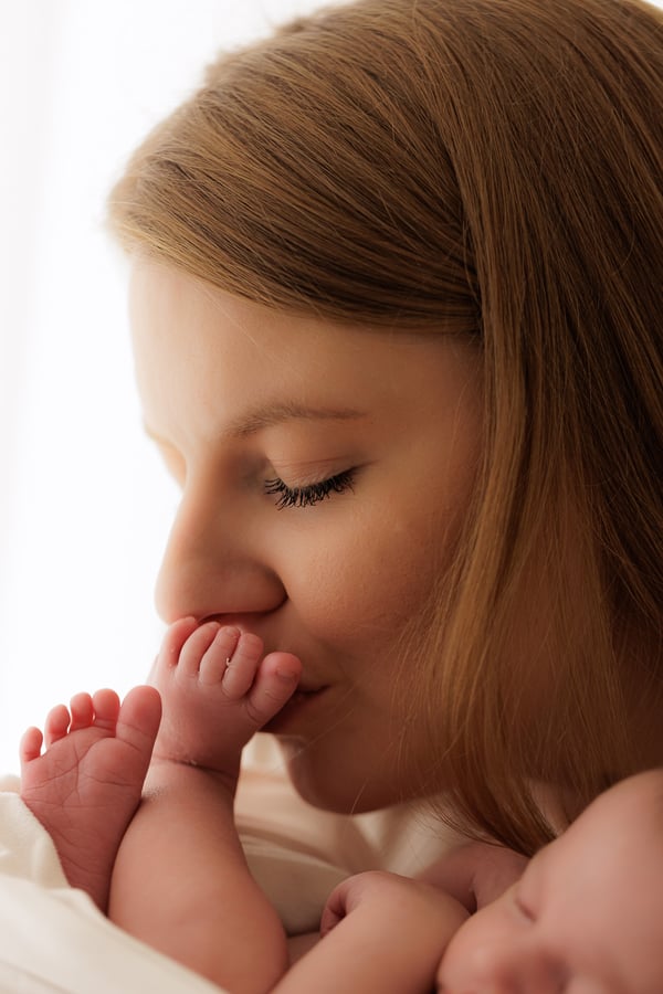 A mother holding her newborn's foot to her lips and kissing it