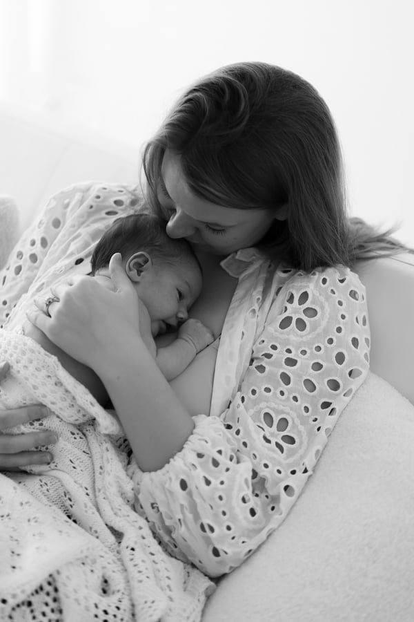 A mother kissing her newborn's head beside a bright window, in black and white