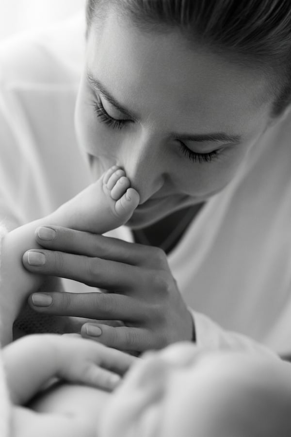 A mother kissing her newborn's foot, in black and white