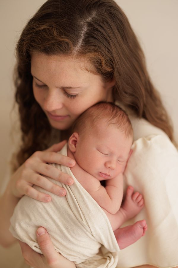 A mother holding her swaddled newborn in both arms and looking down at them