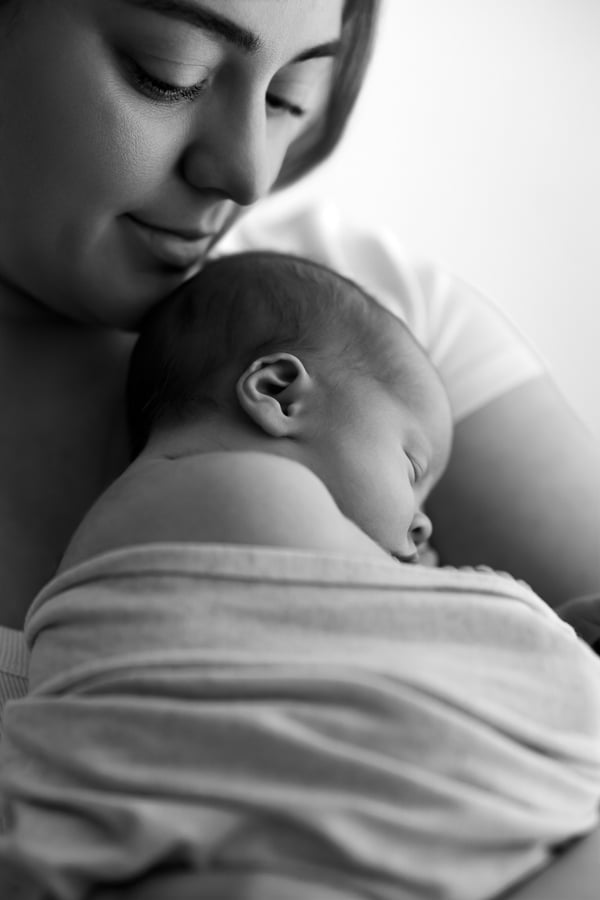 A mother looking down at her sleeping newborn, held against her shoulder