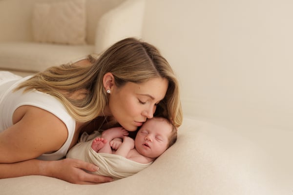 A mother lying down and kissing her swaddled newborn's head
