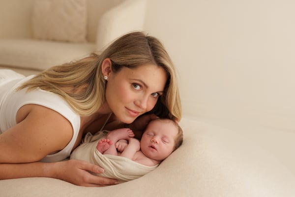 A mother lying beside her swaddled newborn and looking up at the camera