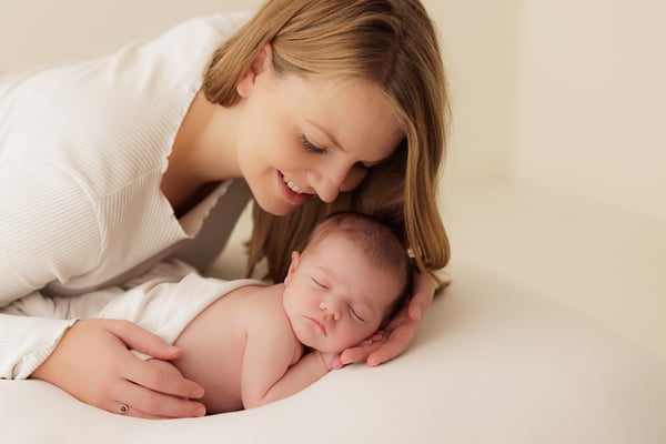 A mother lying down beside her sleeping newborn on a cream beanbag