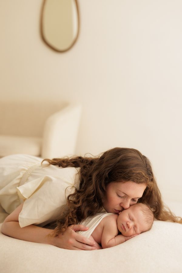 A mother lying down and kissing her newborn, the studio room visible behind