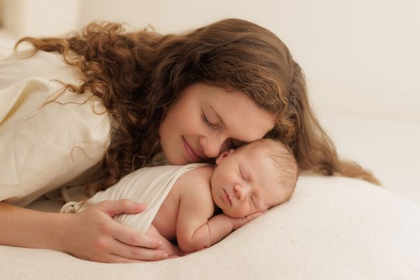 A mother lying down with her cheek resting against her sleeping newborn
