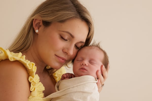 A mother resting her cheek on her newborn's head, both with their eyes closed