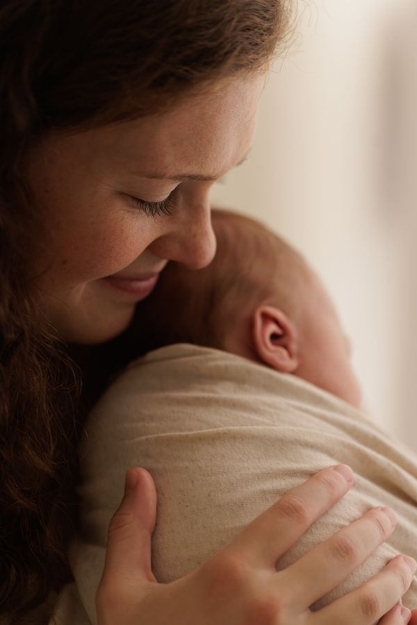 A mother resting her face behind her swaddled newborn's head, both in profile
