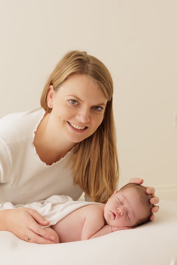 A mother smiling at the camera with a hand resting on her sleeping newborn
