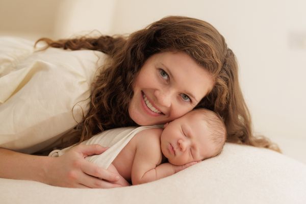A mother lying beside her sleeping newborn and smiling at the camera