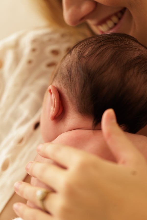 A mother smiling with her hand resting on her newborn's head, seen close in