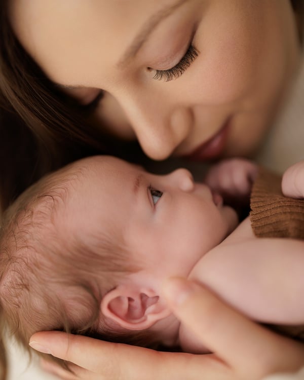 A mother leaning over her newborn, awake with eyes open, cradled in her hands