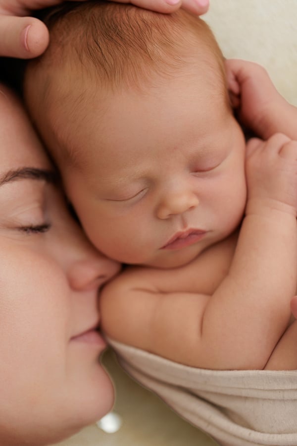 A mother's face pressed against her sleeping newborn's cheek
