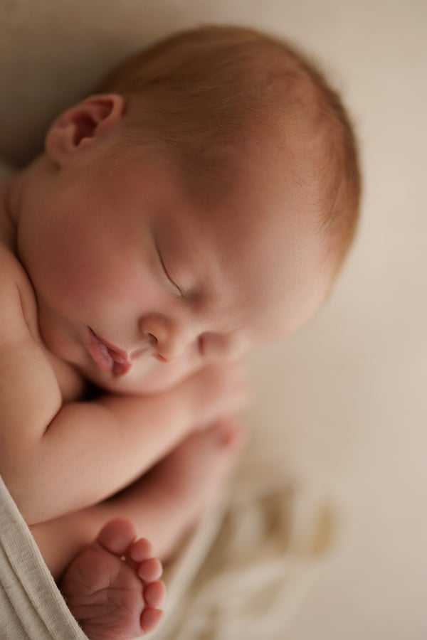 A newborn asleep curled on their side, one foot showing beyond the wrap
