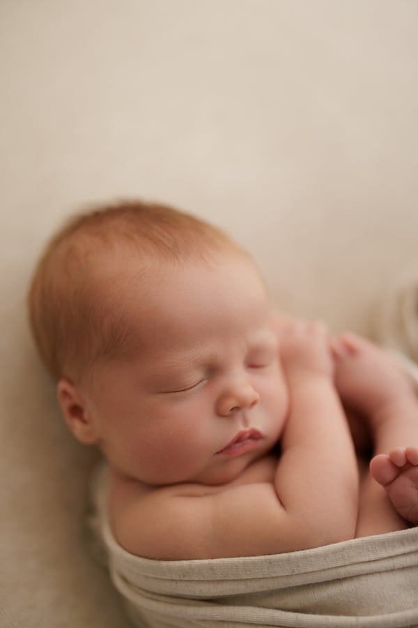 Newborn asleep in a cream wrap on a warm cream backdrop
