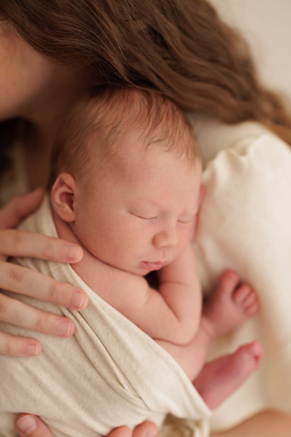 A newborn asleep in a cream wrap, held in their mother's arms
