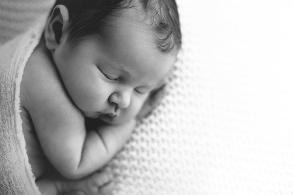 Newborn asleep on a textured knitted blanket, seen in profile, in black and white