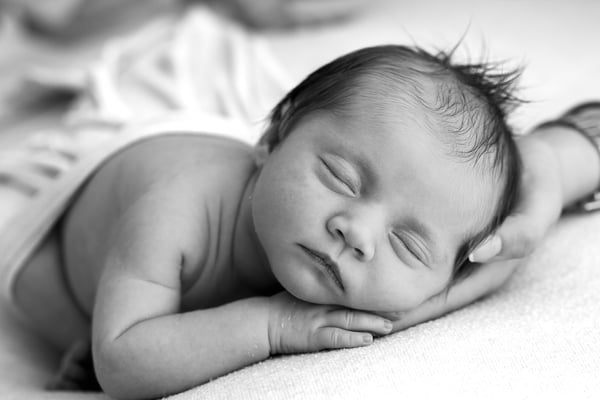 A newborn asleep on a pale blanket, seen close, in black and white