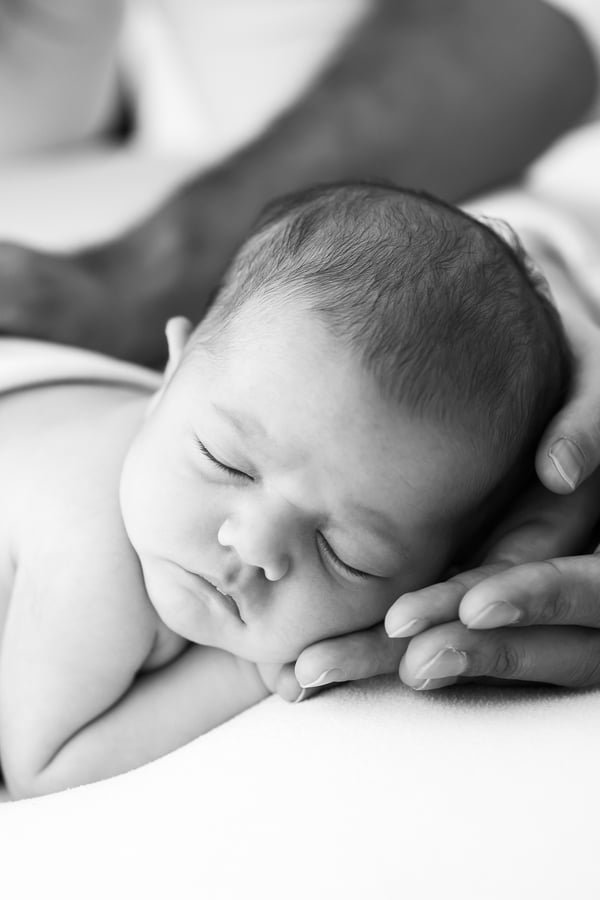 A newborn asleep with their head resting on a parent's hands, in black and white