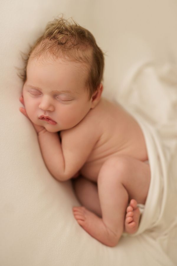 Newborn asleep on their side on a cream backdrop