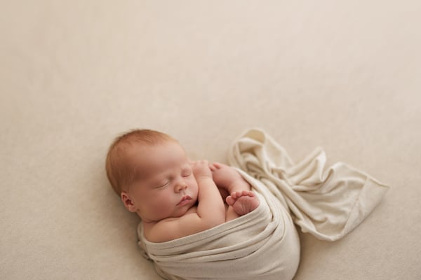 A newborn asleep in a cream wrap, small in a wide and otherwise empty frame
