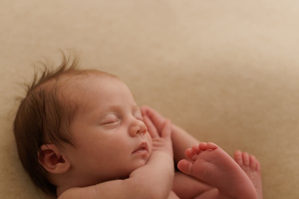 A newborn asleep with both feet drawn up close to her