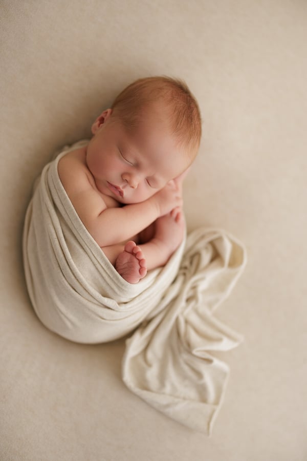 A newborn asleep in a cream wrap, seen from above on a cream blanket