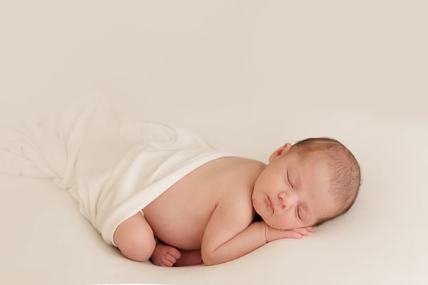 A newborn curled asleep in a cream wrap on a cream backdrop