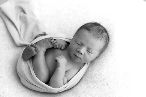 A newborn curled asleep in a loose wrap on a white blanket, in black and white