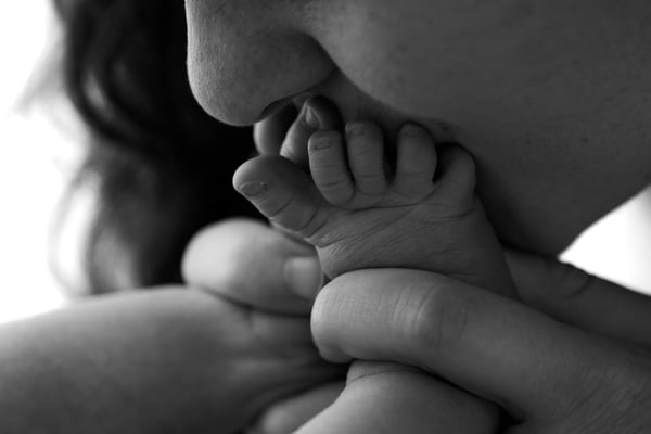 A newborn's feet held in a mother's hands against her chin, in black and white