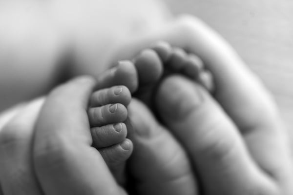 A newborn's feet resting in cupped adult hands, in black and white