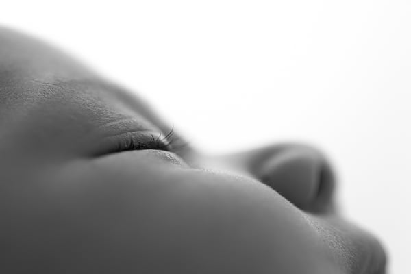 Extreme close-up of a newborn's lips and chin against a bright background, in black and white