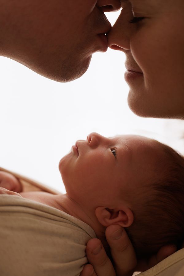 A newborn looking upward while their parents kiss above them