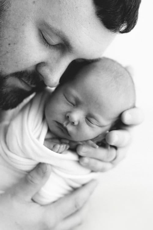 A parent holding a swaddled newborn cheek to cheek, both with eyes closed