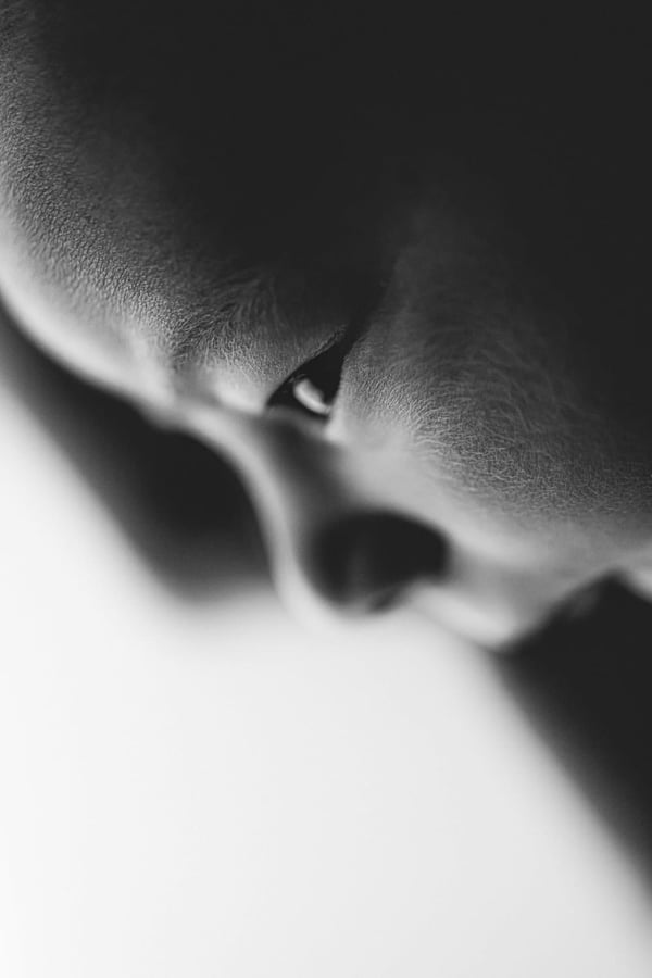 A parent leaning in to kiss a newborn on the head, backlit against white