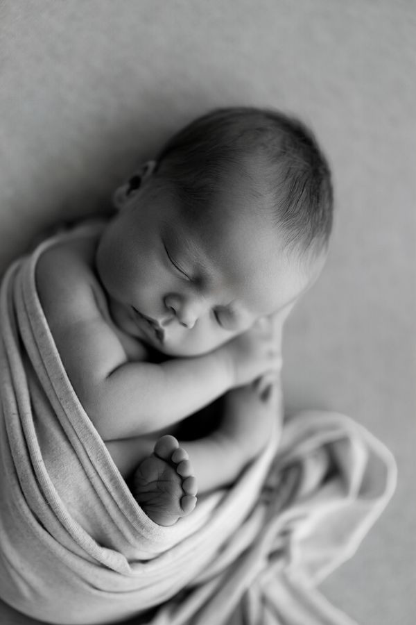 Newborn curled up in a wrap on a grey backdrop, one foot showing, in black and white