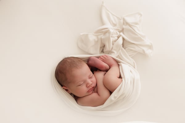 A newborn wrapped and asleep, small within a bright frame, the wrap fanned out beside them