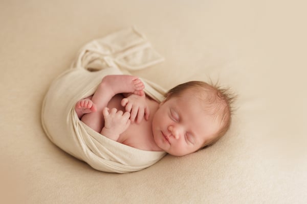A newborn asleep in a cream wrap with both feet showing