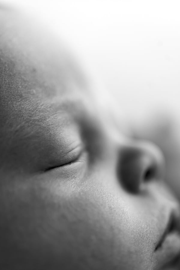 Macro of a sleeping newborn's closed eye and nose against a bright background