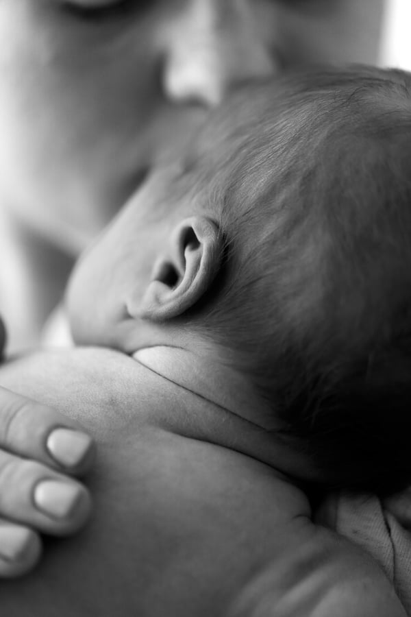 A sleeping newborn's head and ear resting against a parent's shoulder, one tiny hand curled below
