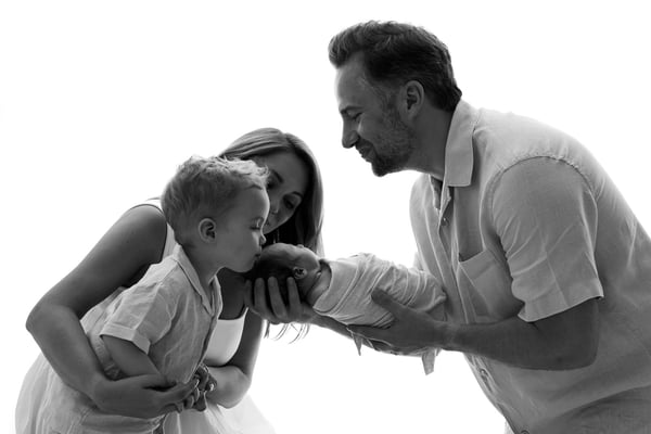 Both parents and the big brother together against a bright window, in black and white