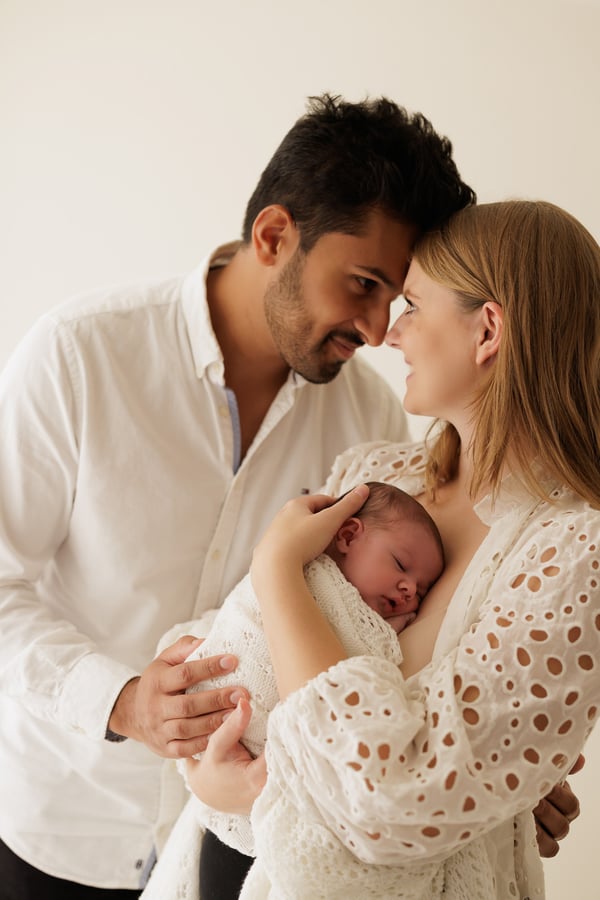 Both parents with their heads together above their swaddled newborn