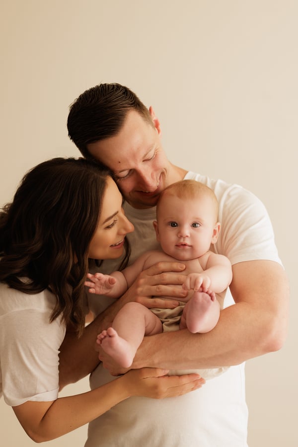 Both parents holding their baby, the father kissing the mother's head