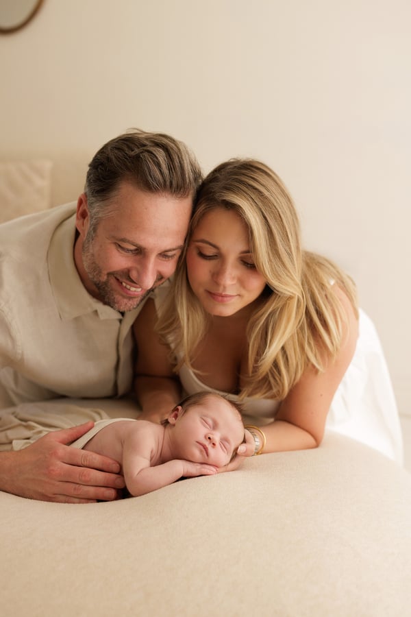 Both parents lying down and looking at their sleeping newborn