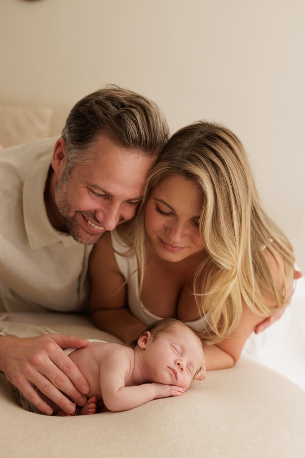 Both parents lying down behind their sleeping newborn