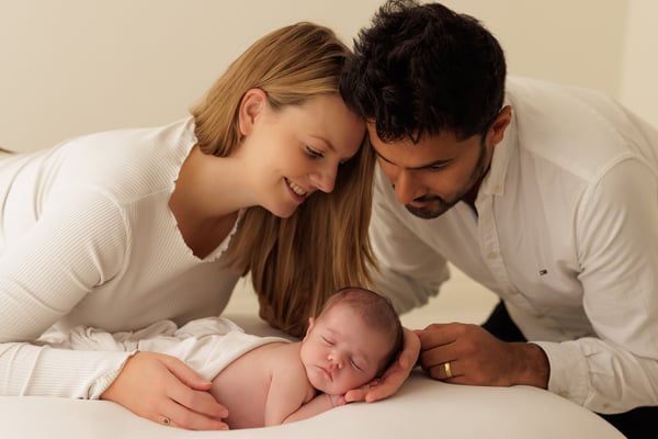 Both parents lying down on either side of their sleeping newborn