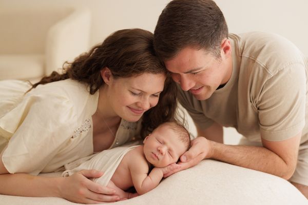 Both parents lying down on either side of their sleeping newborn