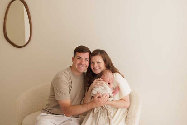 Both parents seated together in the studio holding their newborn, a round mirror on the wall behind
