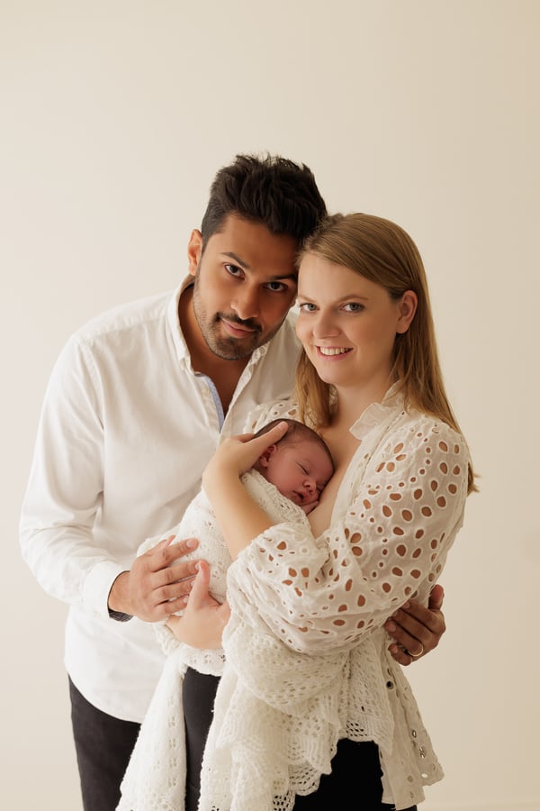 Both parents standing together holding their swaddled newborn and looking at the camera